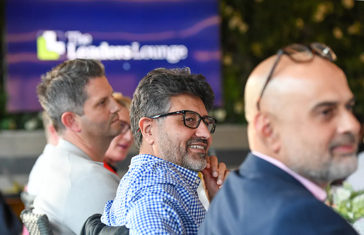 Three guests listening and smiling at the dinner table, with The Leaders' Lounge logo glowing on the screen behind them.
