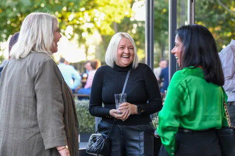 Three guests laughing together by the open doors, glasses in hand.