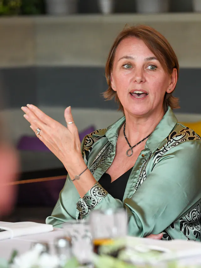 A woman in a green satin blouse gesturing as she makes a point to the table.