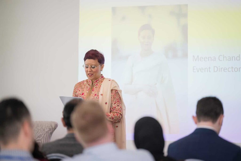 Meena-Chander-addresses-the-audience | Business MK Woman in a pink embroidered traditional outfit delivers a talk at a podium, audience visible in the foreground.