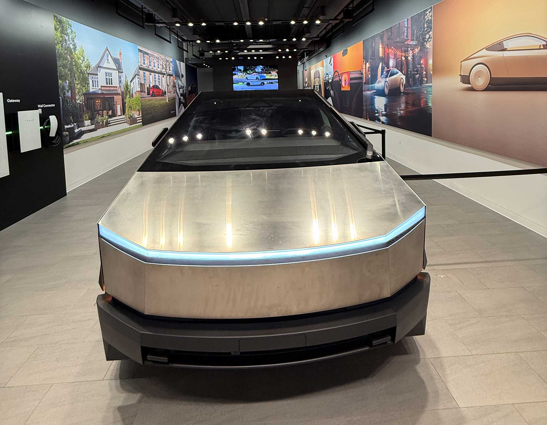 Front view of a silver, angular concept car on a display pedestal in an indoor showroom with wall murals behind