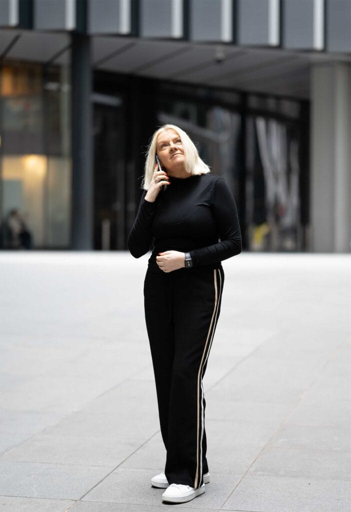 Justine Maroudias on modern leadership | Business MK Woman with blonde hair in a black outfit talking on a cellphone outside, near a modern building.