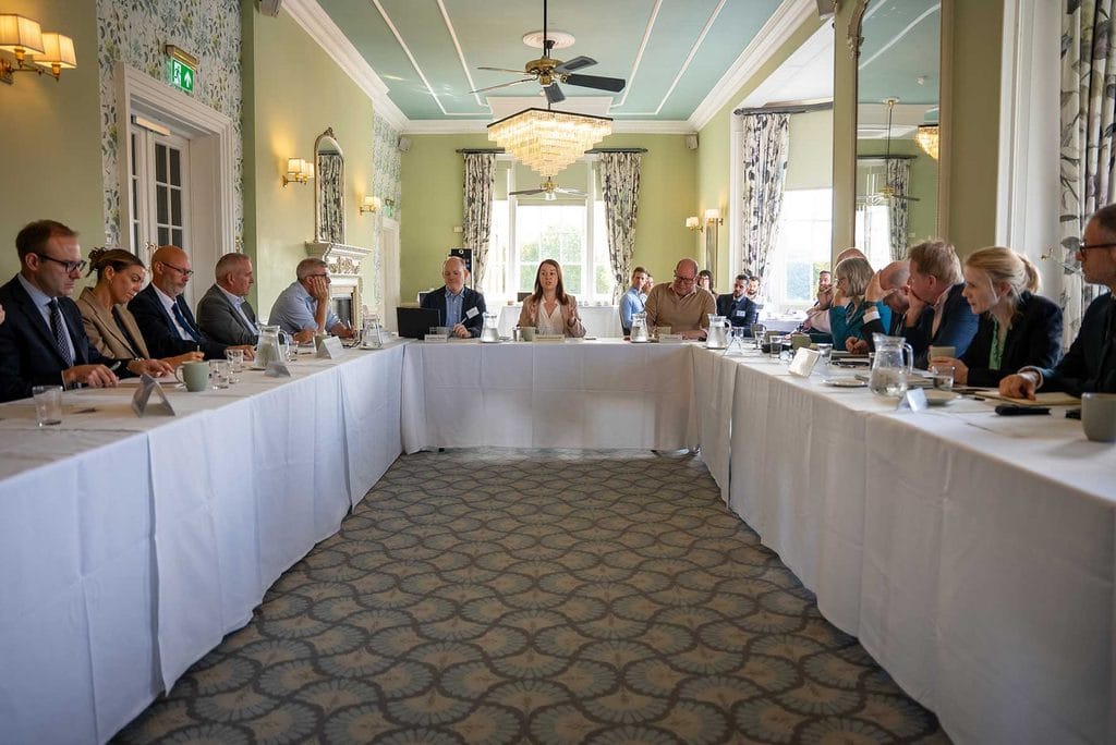 Tourism-Minister-attends-Universal-Studios-Roundtable | Business MK Business meeting in a sunlit, U-shaped room with people seated around long white-clothed tables joining for discussion.