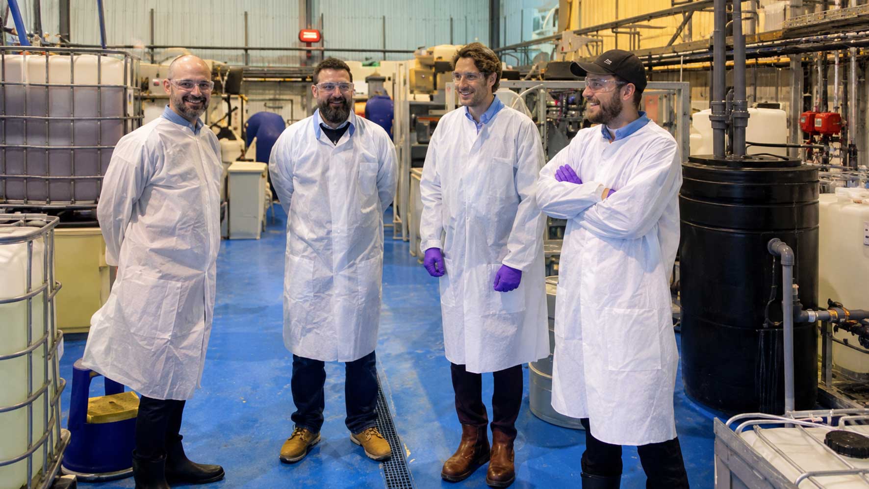 Four people wearing laboratory coats inside an industrial facility, illustrating technical support for climate technology businesses.