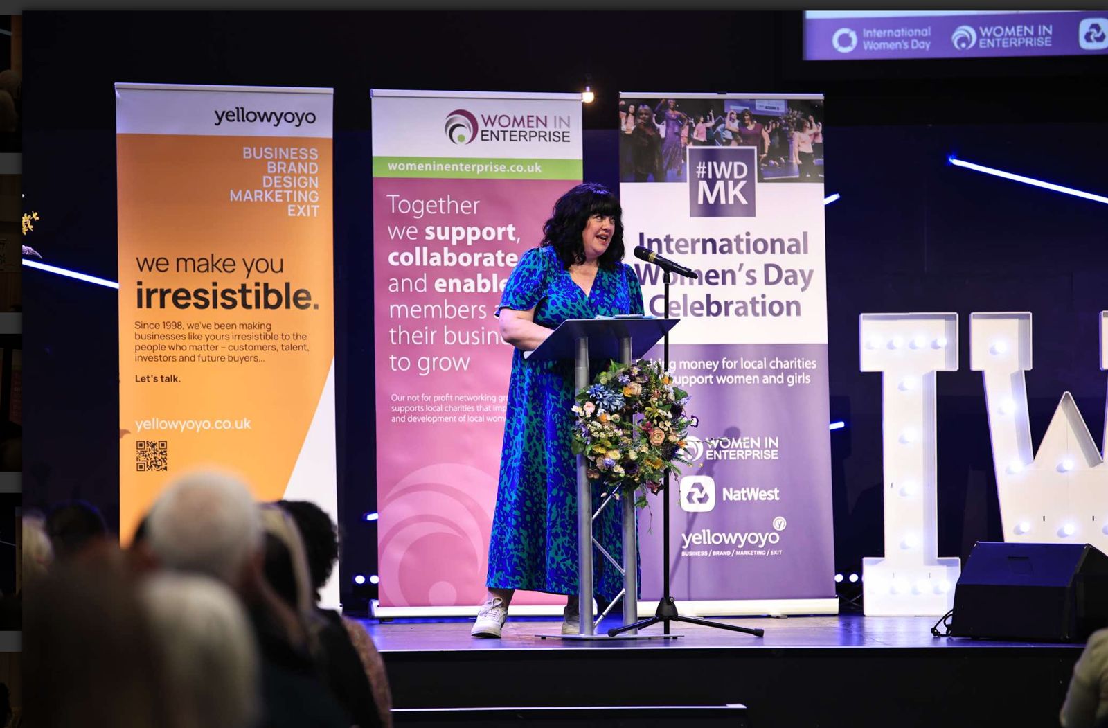 Michelle Theuma speaking on stage at International Women's Day Milton Keynes 2026, organised by Women in Enterprise.