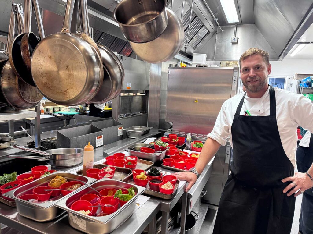 ben-francis-head-chef-cherry-tree-olney-kitchen | Business MK Ben Francis, Senior Head Chef at The Cherry Tree in Olney, standing in the restaurant kitchen beside a selection of prepared ingredients.